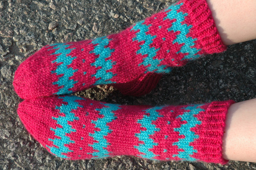 Iida-neulesukat, joissa on pinkki-turkoosi-sahalaitakuvio henkil&ouml;n jaloissa.