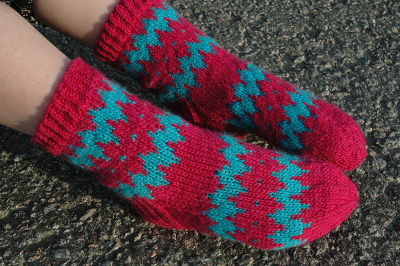 Iida-neulesukat, joissa on pinkki-turkoosi-sahalaitakuvio henkil&ouml;n jaloissa.