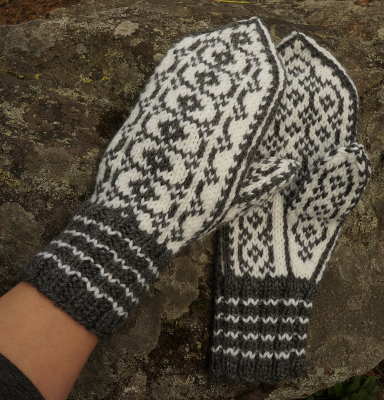 Valkoharmaat Riimu-kirjoneulelapaset. Toinen henkilön k&auml;dess&auml;, toinen kalliolla.